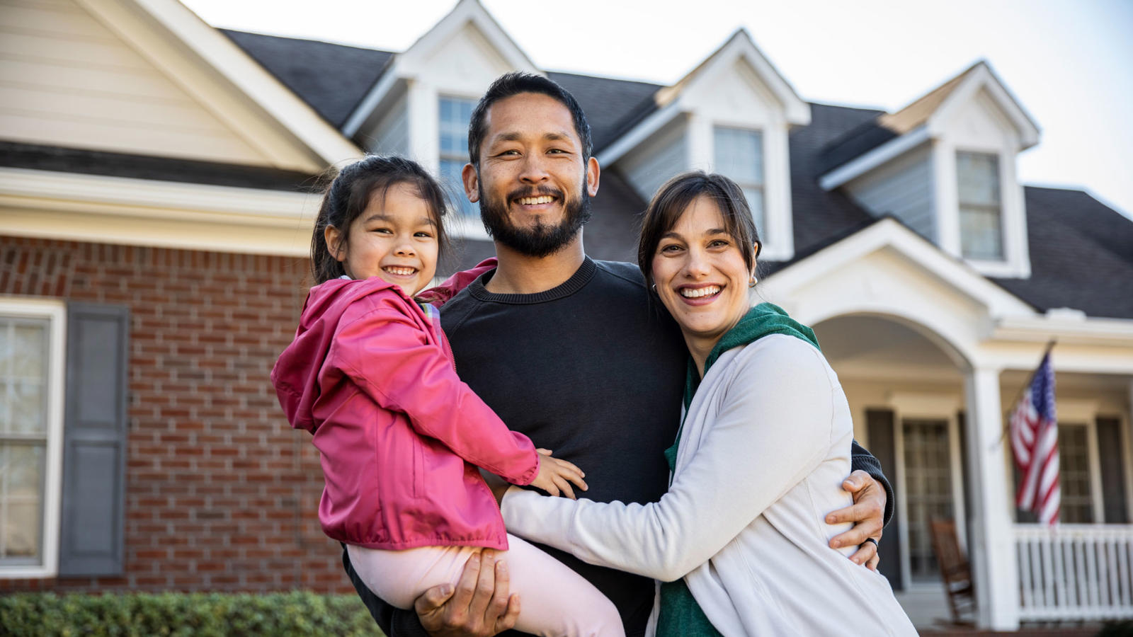 a man and woman holding a child in front of a house