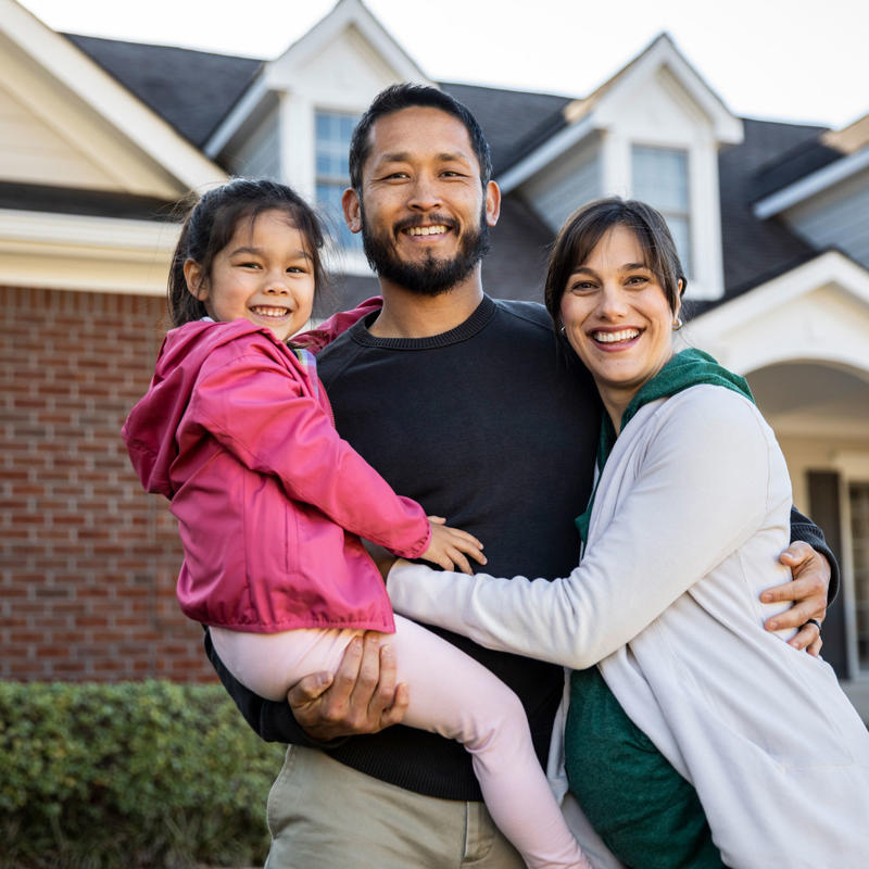a man and woman holding a child in front of a house