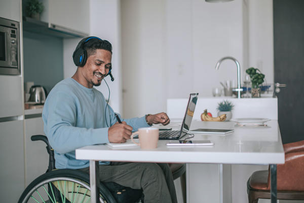 a man in a wheelchair wearing headphones and using a laptop