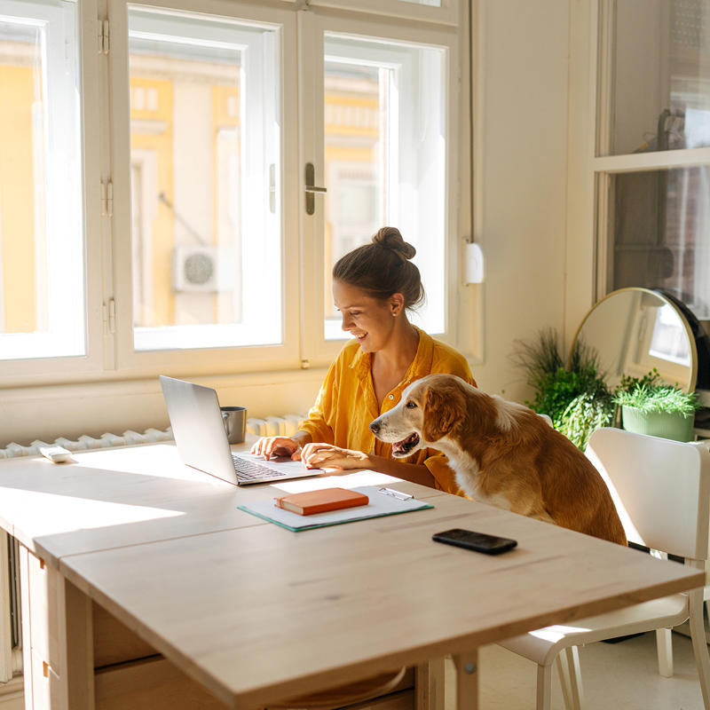 A woman works on her laptop at a table next to her dog.