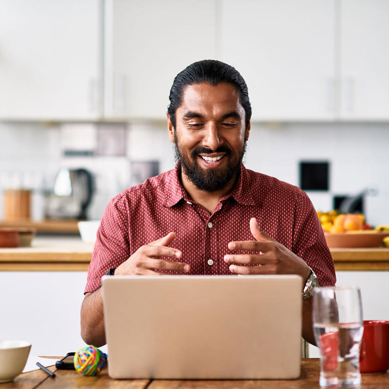 A man sits in his kitchen while working on his laptop.