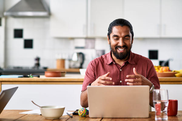 A man sits in his kitchen while working on his laptop.